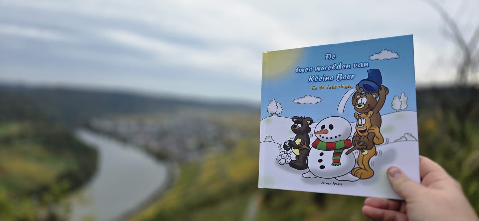 Het hardcover-boek van Kleine Beer in de hand, tegen een landschap
